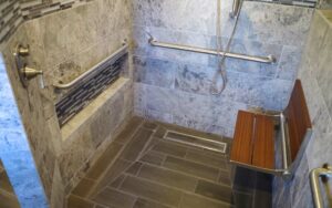 A custom tiled barrier-free shower stall with built-in hand rails, grab bars, and a fold-down shower seat.