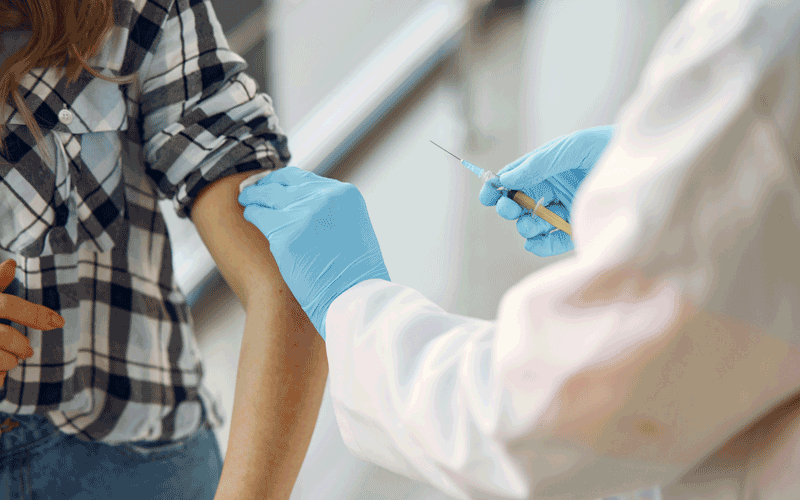 photo of a woman's arm with a rolled up sleeve as a nurse wearing blue latex gloves administers a vaccine shot